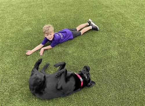 kid lying on turf of playground with dog laying on its back beside him