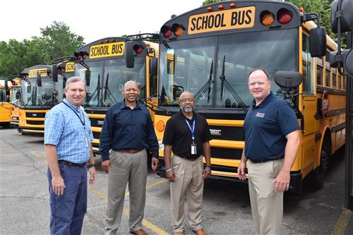 Travis Schrimsher welcomed as transportation administrator by several Madison City Schools administrators beside schoolbus