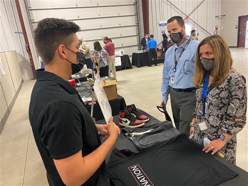 Student at his sports apparel booth talking with two onlookers