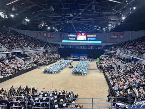 far away pic of jC graduates seated on floor from back of arena