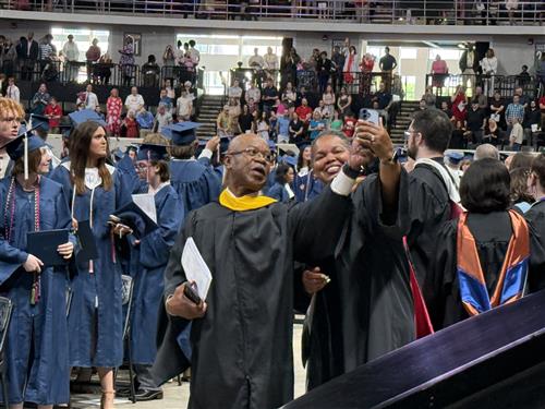 bj faculty in cap and gown with seniors behind them