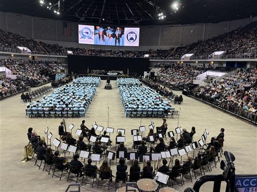 wide angle view of arena with graduates seated in rows beyond band