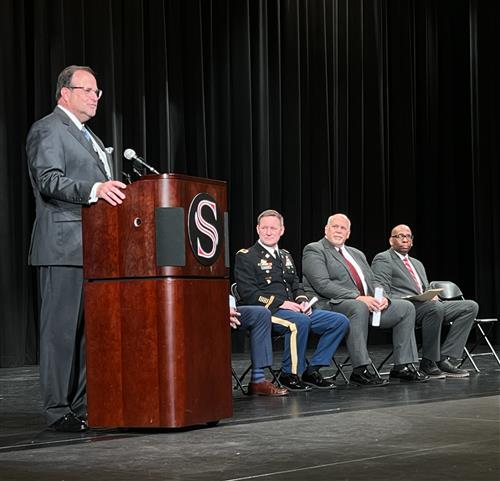 Dr. Nichols at podium with Redstone Arsenal leader and two superintendents beside him