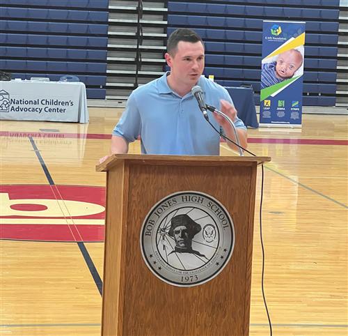 Dustin Haraway at podium in gym addressing audience