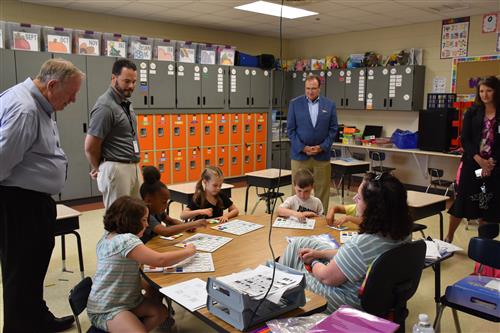 Senator Butler with Board President Tim Holtcamp and Dr. Ed Nichols at table full of students in reading lesson