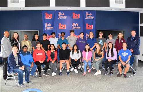 Students seated with principal and superintendent in front of a Bob Jones banner