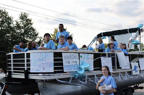 swim and dive team riding in pontoon boat being towed in parade