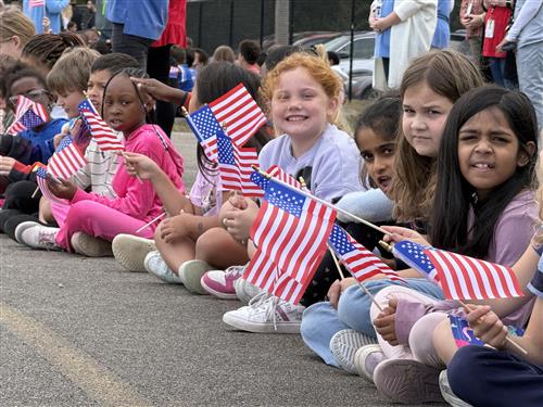 Students lining the curb of a parade route at the school and  holding flags