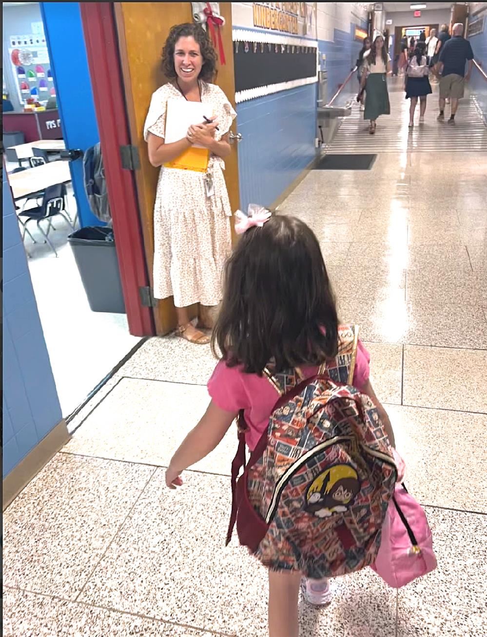  student in backpack greeting teacher at classroom door